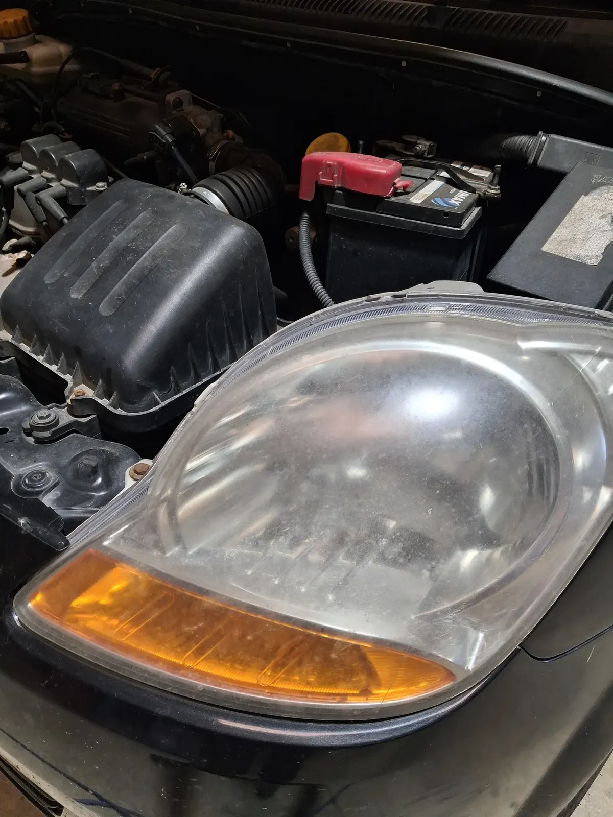 Compartiment moteur ouvert : boîtier de filtre à air, batterie et optique avant d'une voiture en entretien