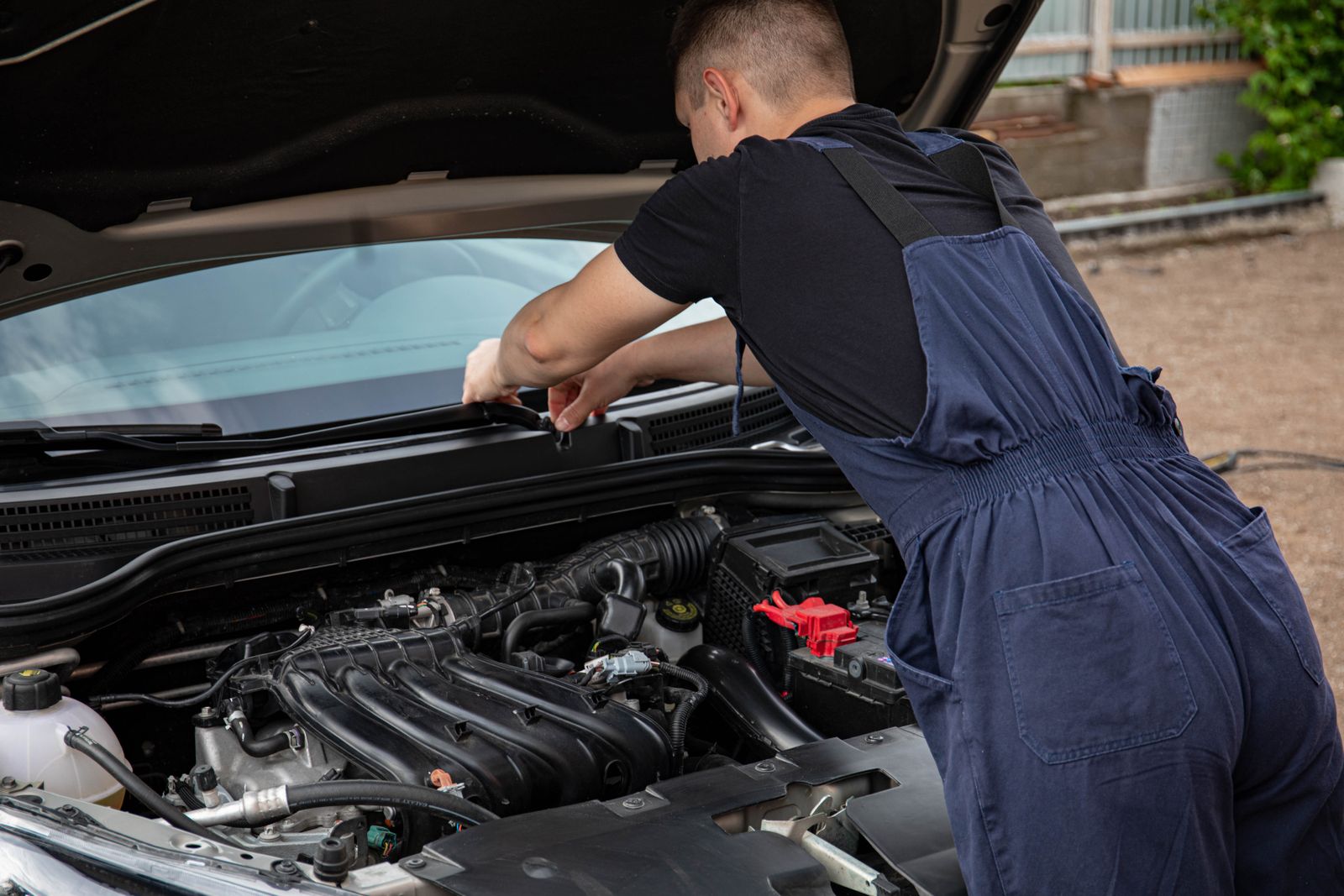Mécanicien en bleu de travail effectuant l'entretien d'un moteur de voiture en extérieur