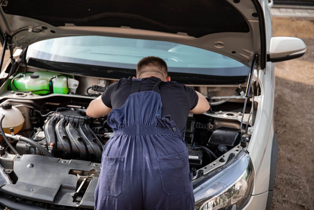 Mécanicien en combinaison travaillant sur le moteur d'une voiture en extérieur